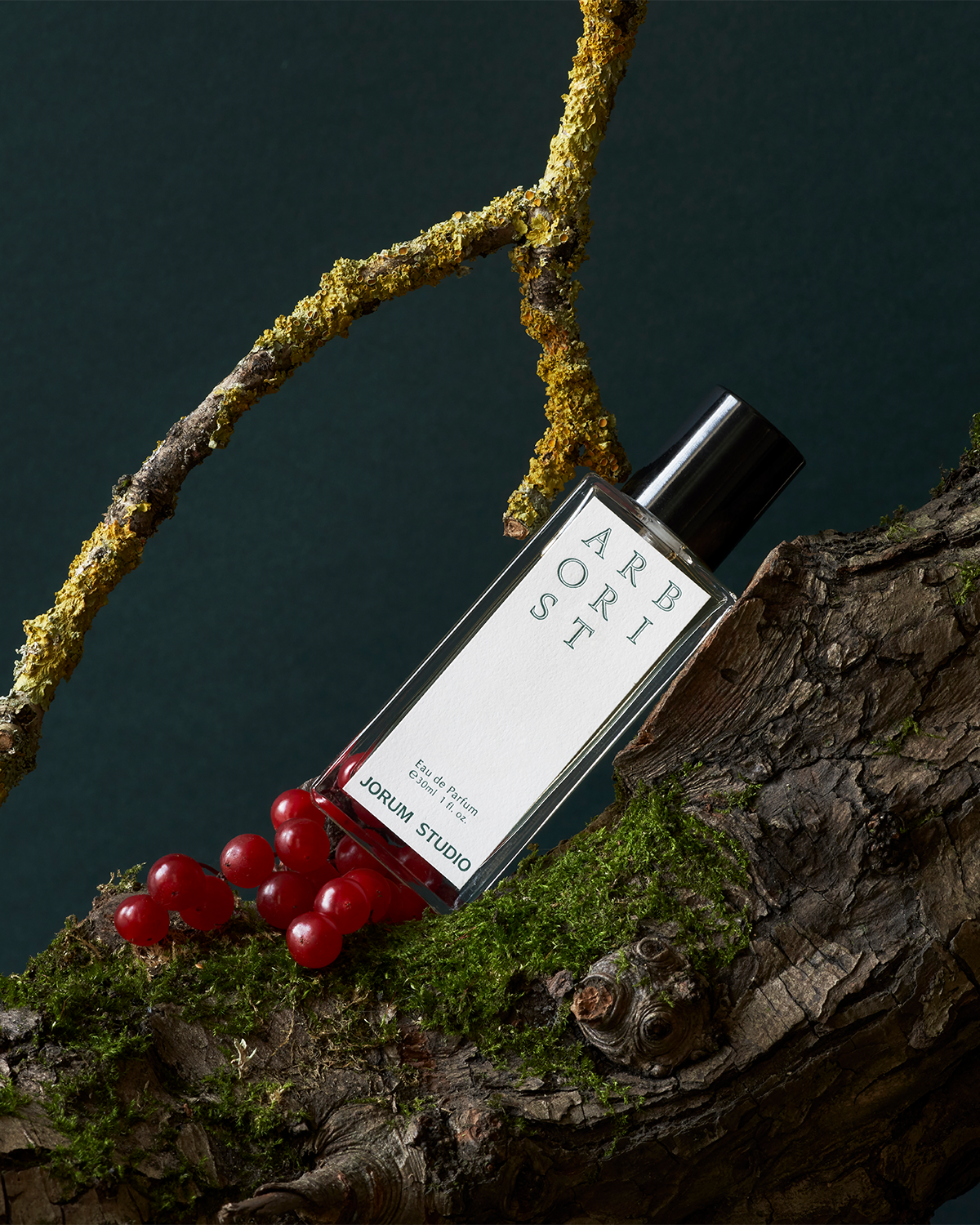 Bottle of Arborist Eau de Parfum by Jorum Studio, arranged in a still-life featuring a mossy branch and red berries