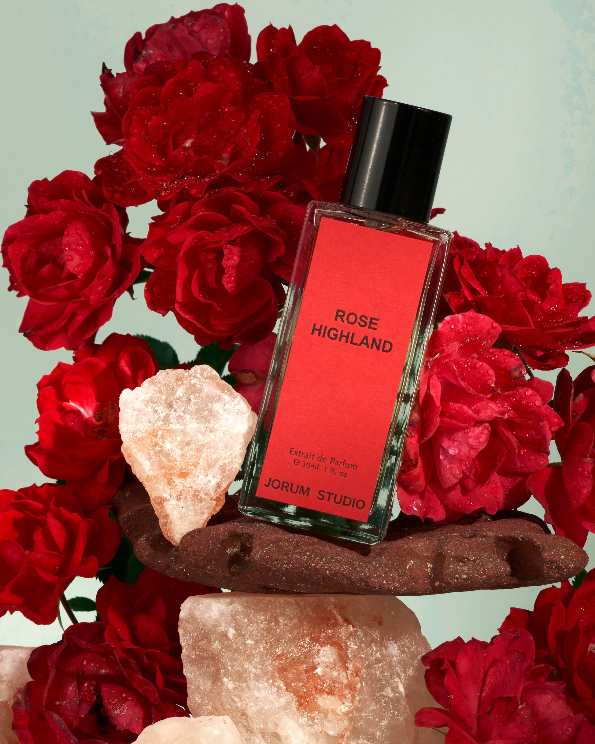 Jorum Studio Rose Highland perfume bottle arranged in a still-life featuring red roses and pink salt crystals