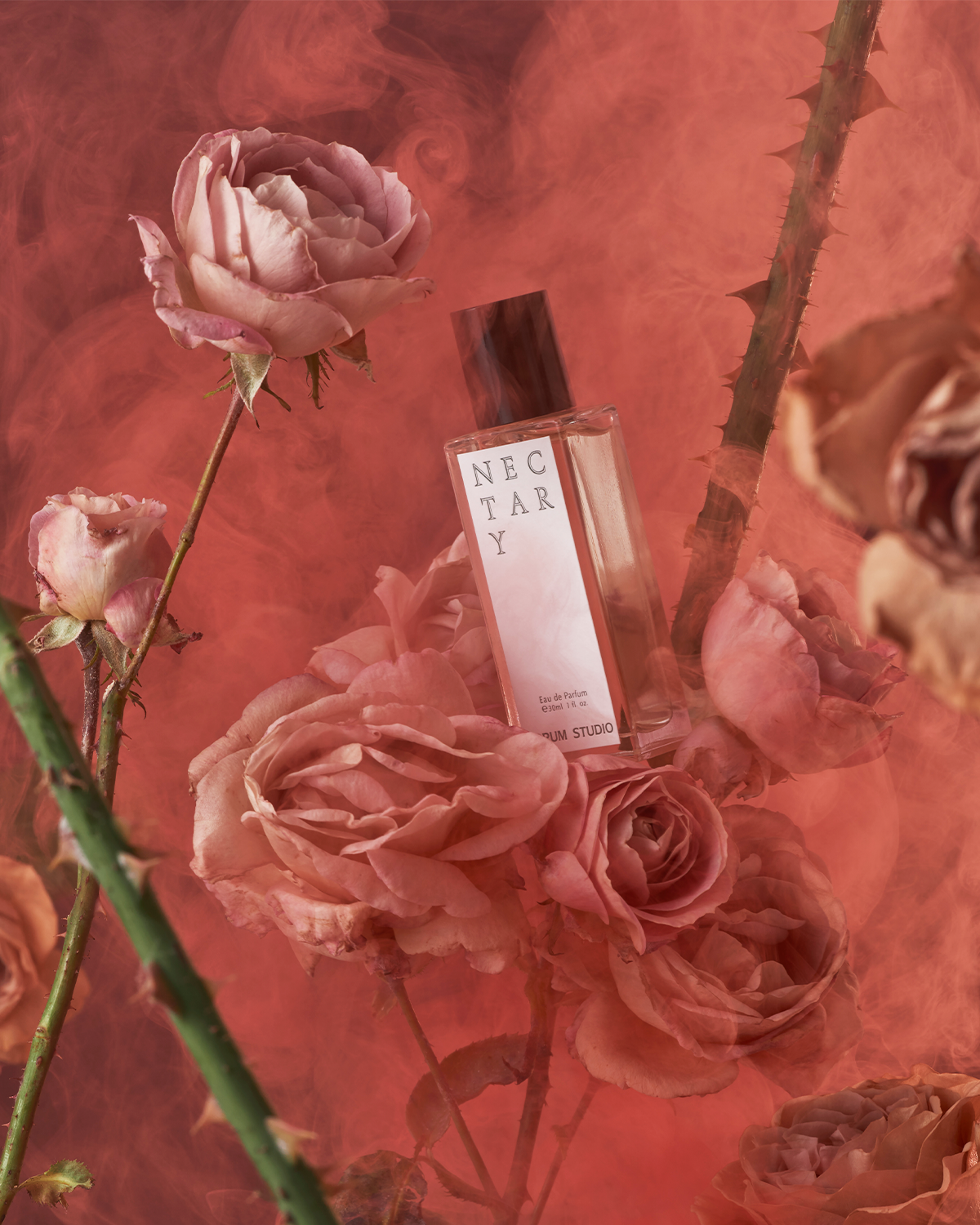 Jorum Studio Nectary perfume bottle arranged in a still-life featuring roses, thorny branches and red smoke