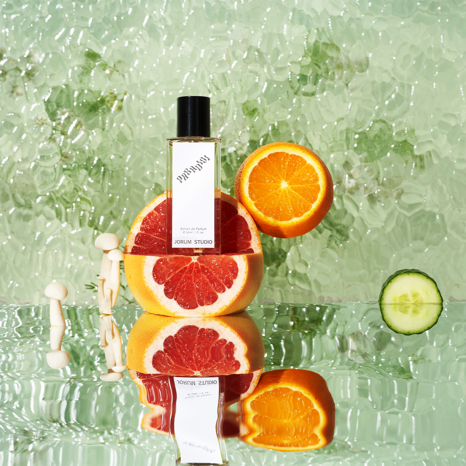 Jorum Studio Paradisi perfume bottle arranged in a still-life featuring grapefruit, orange, cucumber, enoki mushrooms against a watery pale green background
