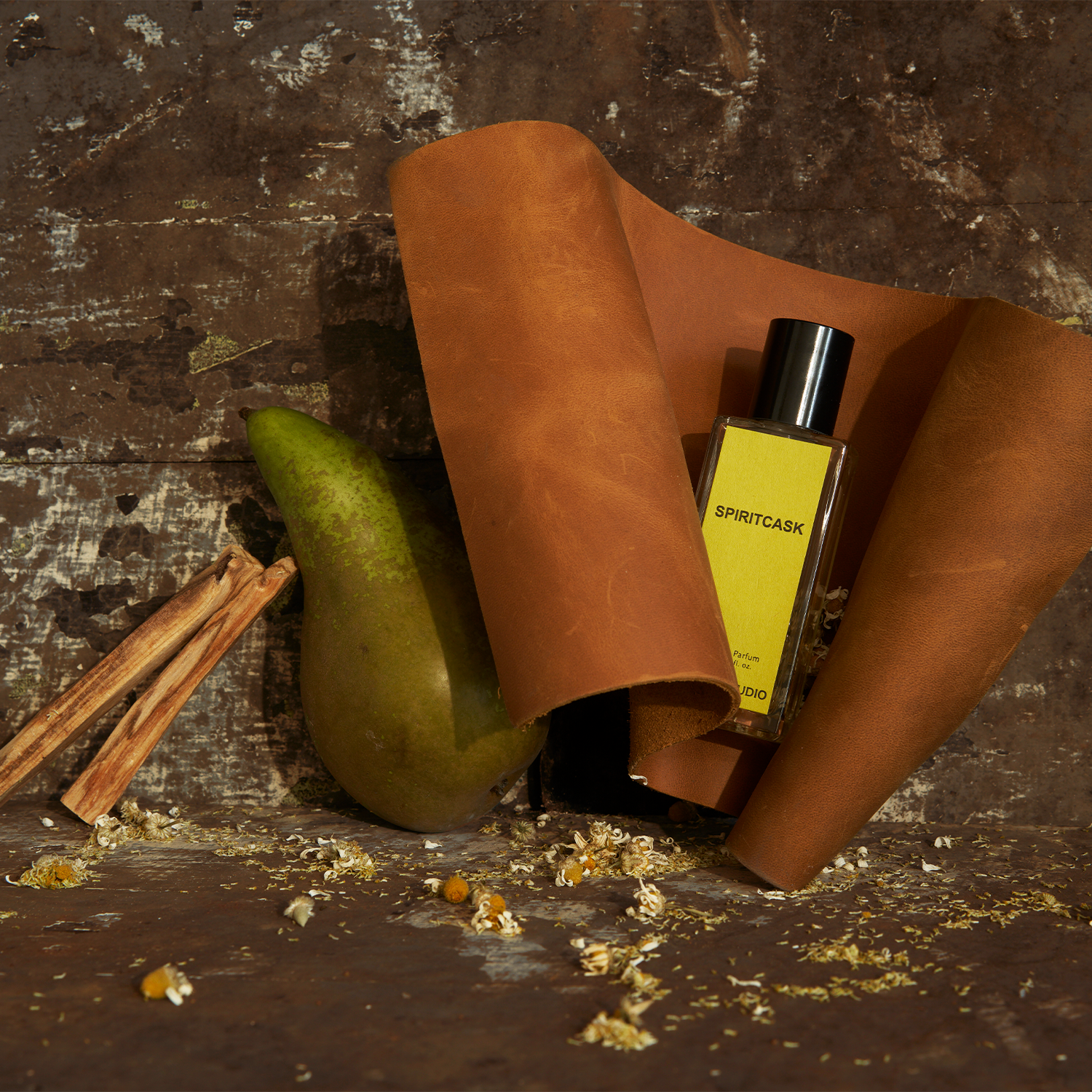 Jorum Studio Spiritcask perfume bottle arranged in a still-life featuring brown leather, a pear, dried chamomile against an aged wooden background