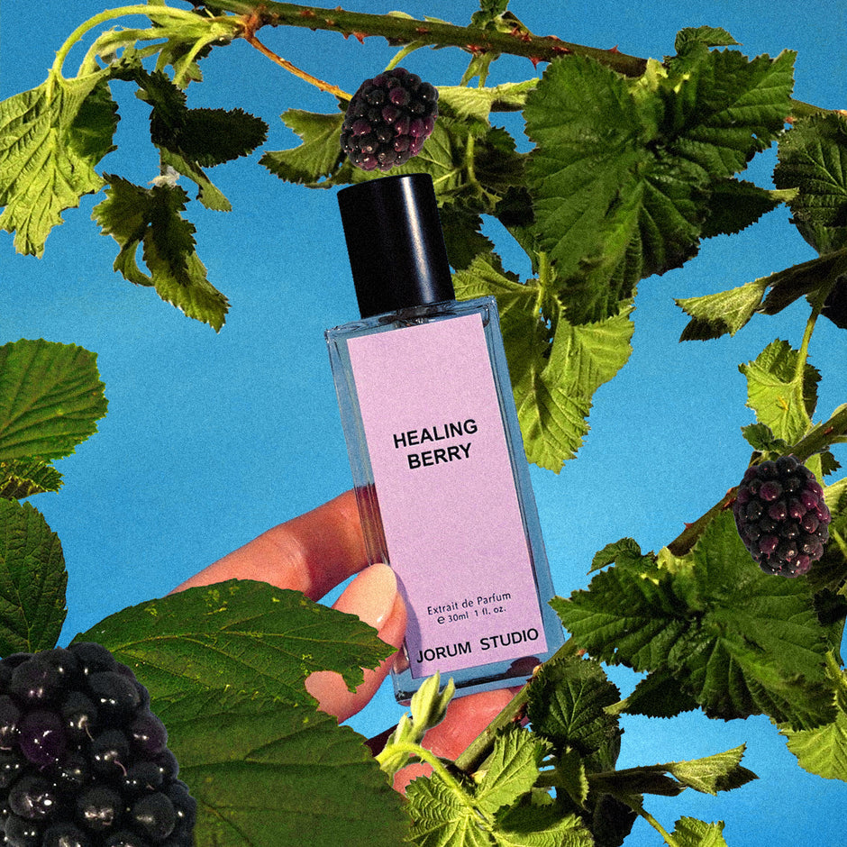 bottle of Jorum Studio healing Berry perfume amongst brambles against a blue sky