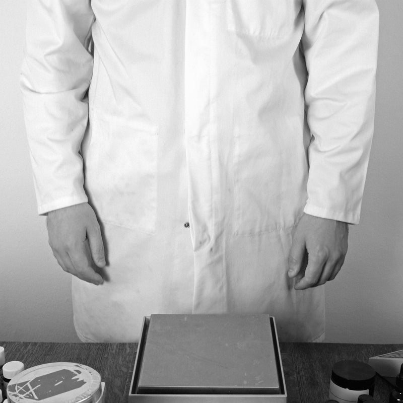 Black and white image of a perfumer standing behind a table with digital scales