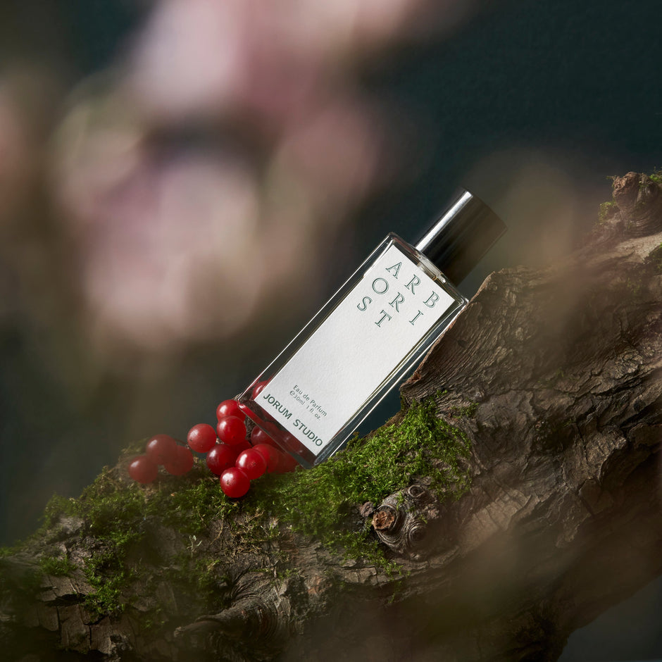 A bottle of Arborist Eau de Parfum by Jorum Studio propped against a mossy log, decorated with red berries