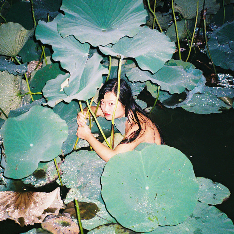Photograph of woman in pond amongst giant leaves by Ren Hang