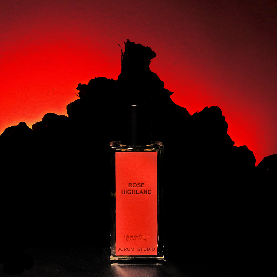 Bottle of Rose Highland perfume in front of silhouette of a mountain with red sky