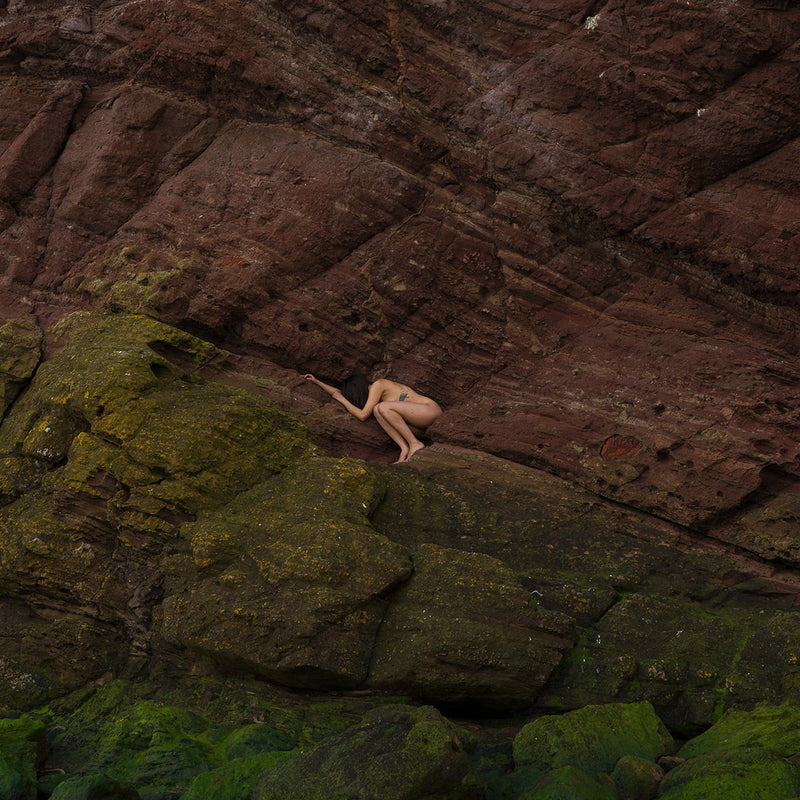 Image of nude figure crouched on mossy rocks by Gabriela Silveira