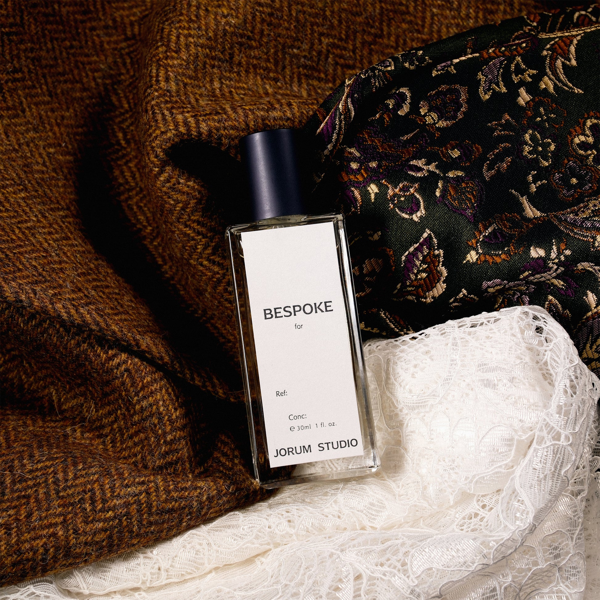 Bespoke Perfume from Jorum Studio sitting on rich fabrics of tweed, silk and lace