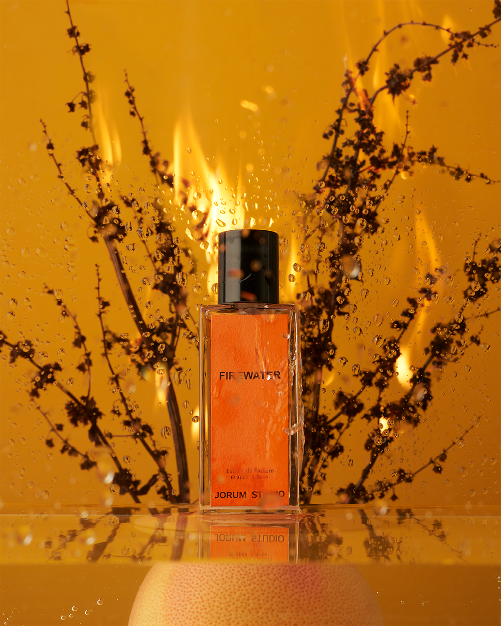 Jorum Studio Firewater perfume bottle arranged in a still-life with burning branches, water reflections and an orange